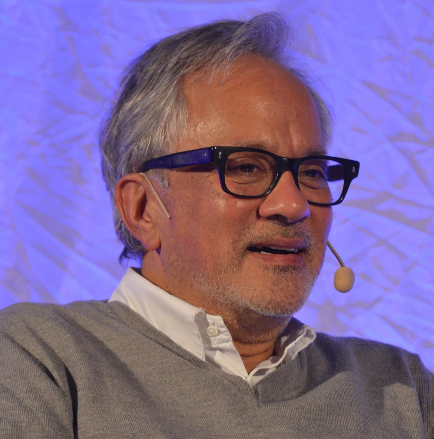 Anish Kapoor in thick black glasses, with a headset microphone.