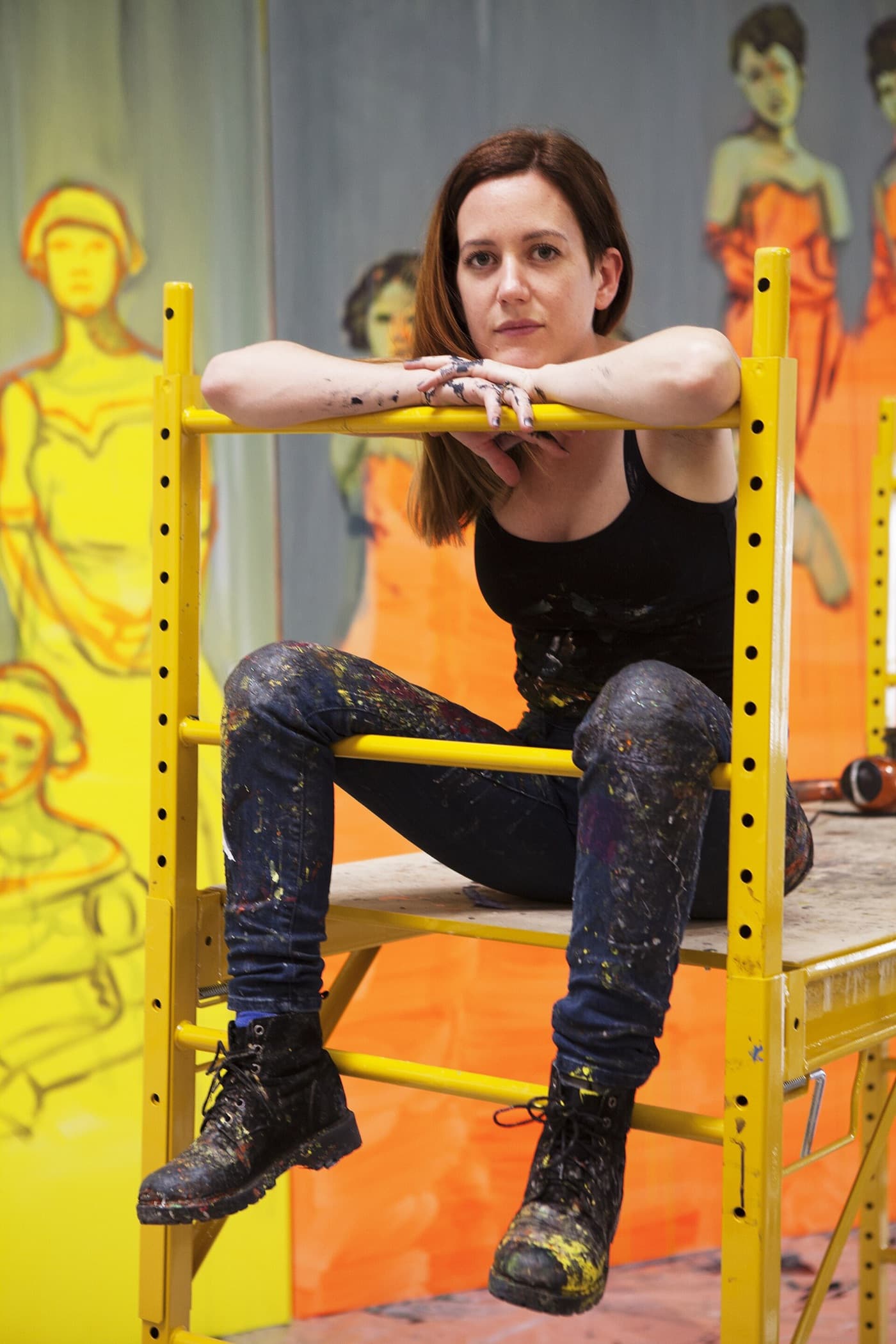 Claire Tabouret resting her arms on a yellow scaffold in front of a painting.