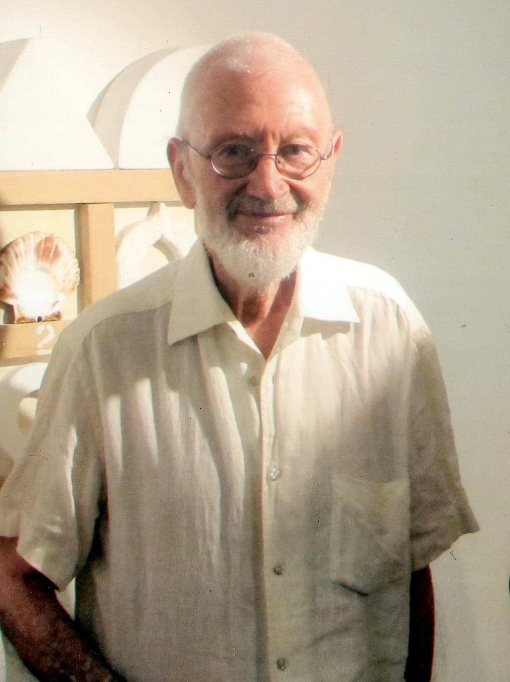 Joe Tilson, white-bearded, in a white shirt in his studio.