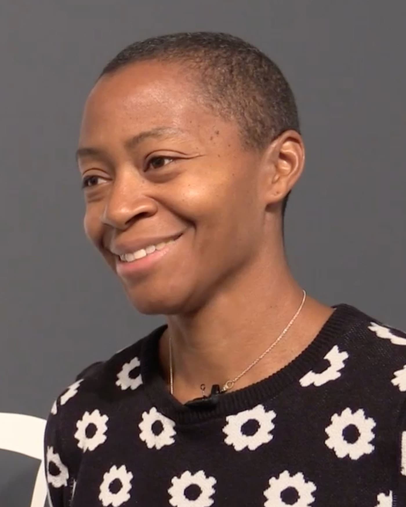 Kara Walker, with short hair, smiling against a grey background.