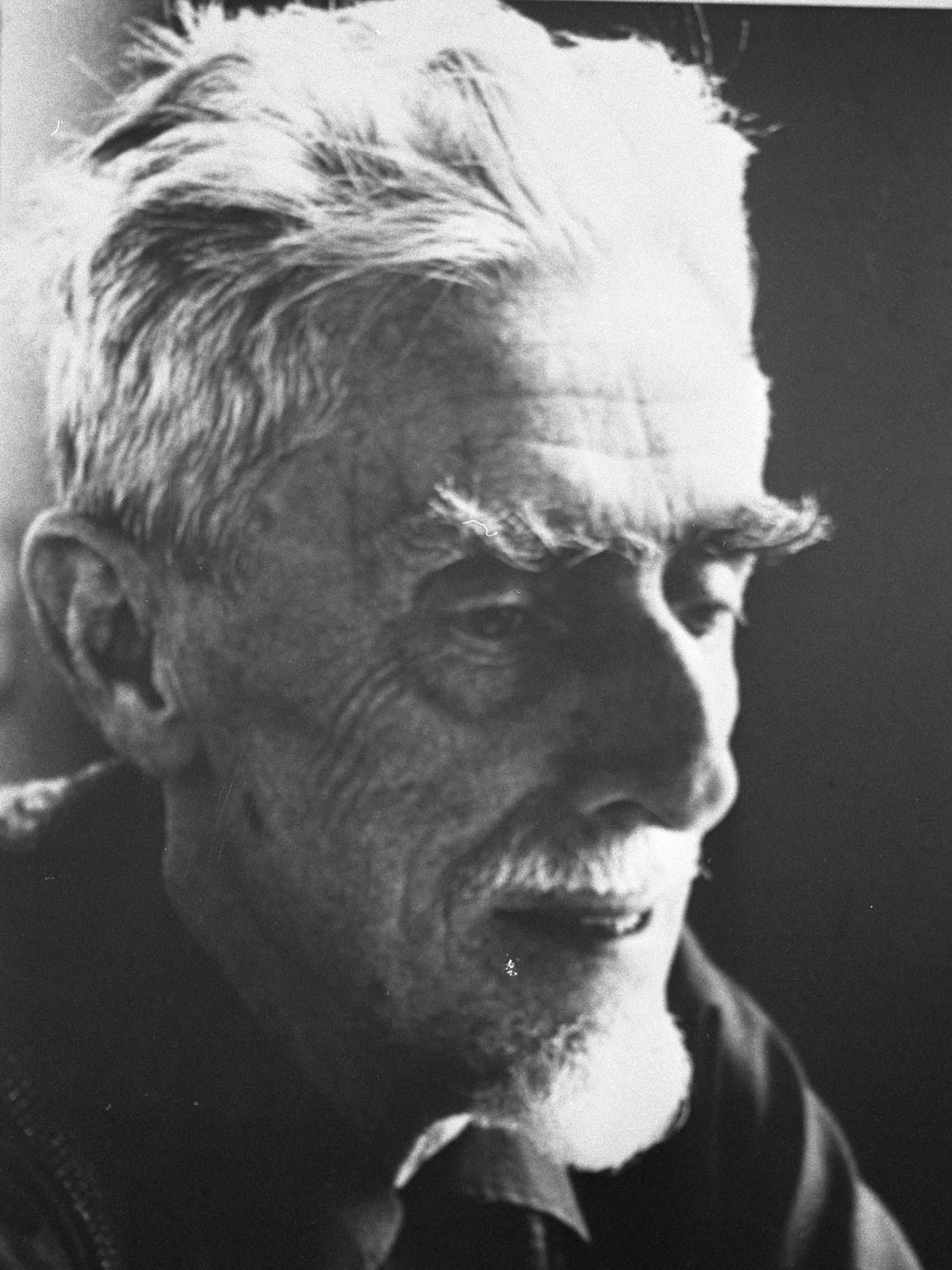 M. C. Escher, close up, with white hair and heavy eyebrows.