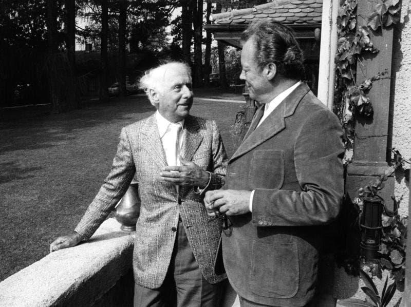 Max Ernst, white-haired, in a tweed jacket, talking with Willy Brandt on a terrace.