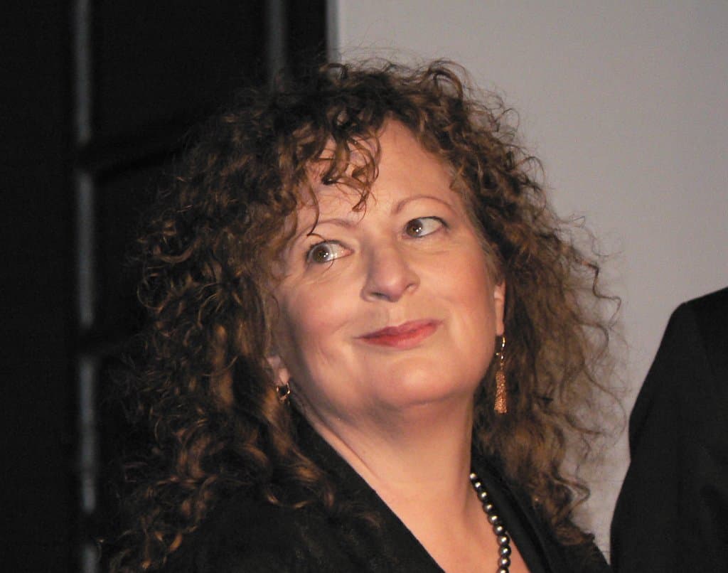 Nan Goldin with curly auburn hair, smiling slightly, in a black top.