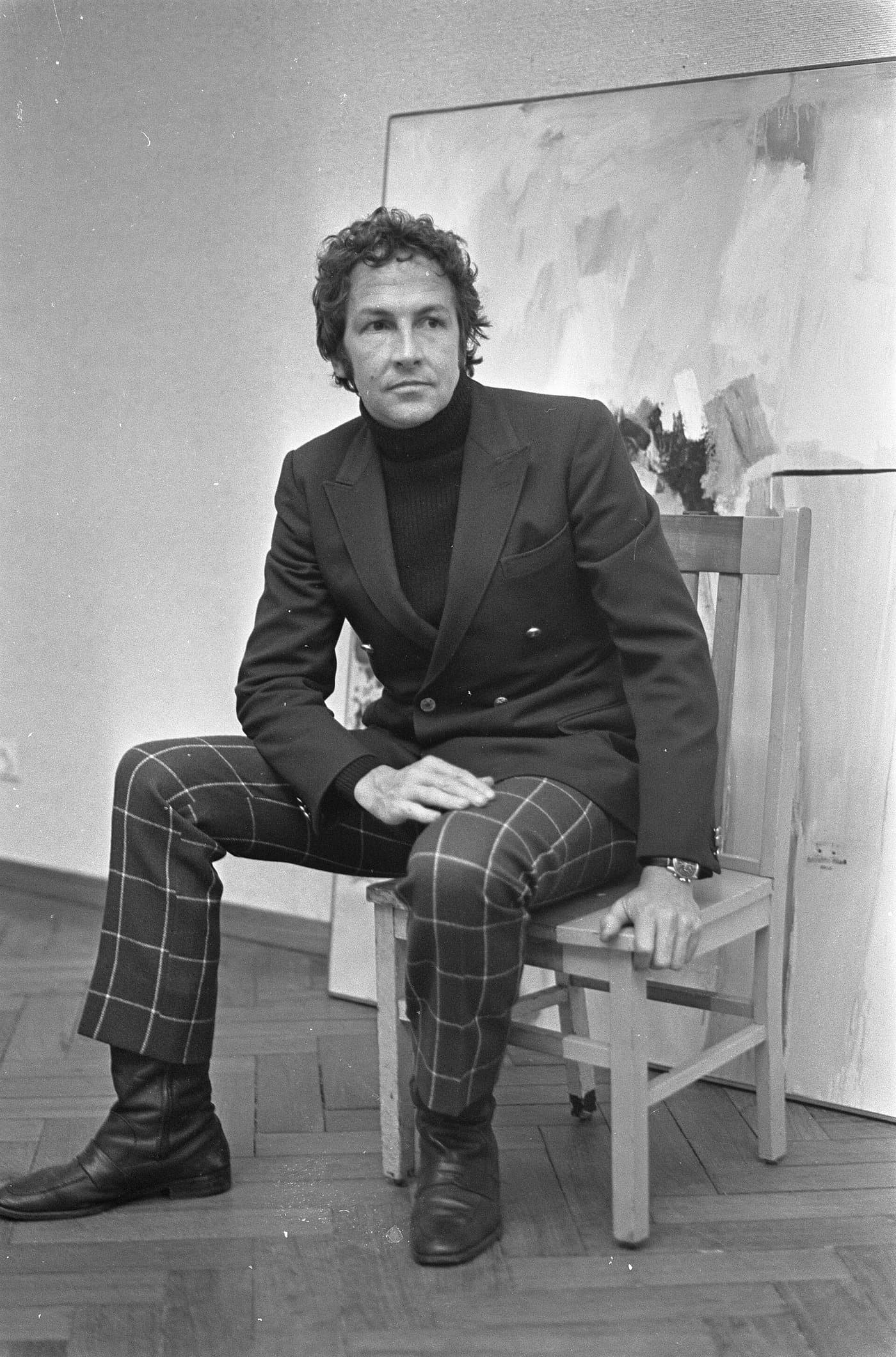 Robert Rauschenberg in a dark suit and polo neck, sitting on one of his own works.