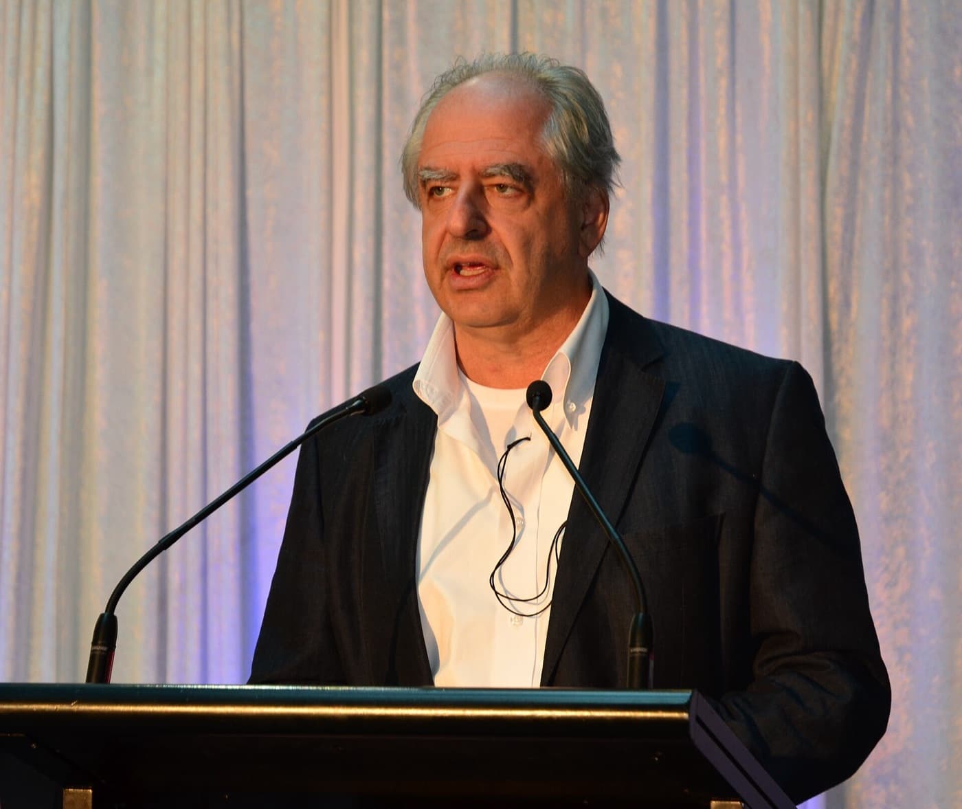 William Kentridge speaking at a lectern in a dark jacket and white shirt.