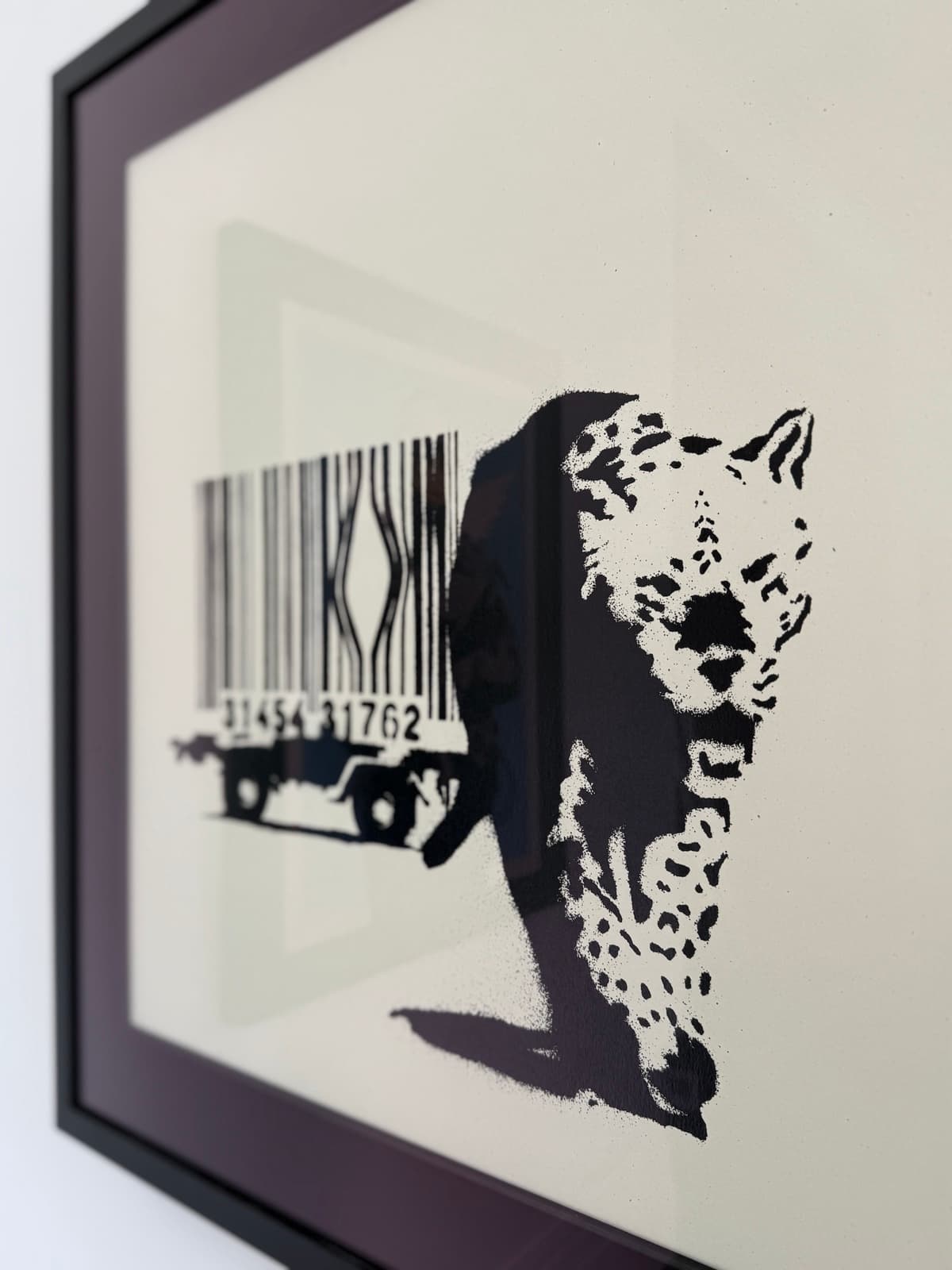 Banksy's Barcode, framed: a leopard stepping out of a broken barcode cage on a trailer, photographed at an angle on a white wall