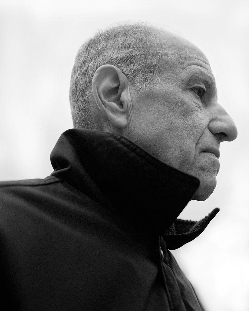 Alex Katz in profile in a dark high-necked jacket, in black and white.