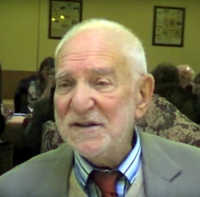Anthony Caro, white-haired, smiling, in a crowded room.