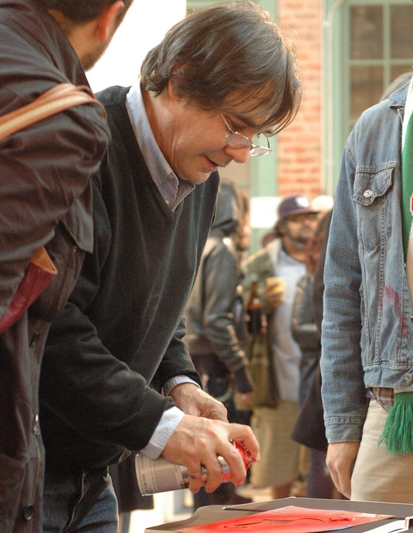 Blek le Rat, in glasses, leaning over a table to sign a book.