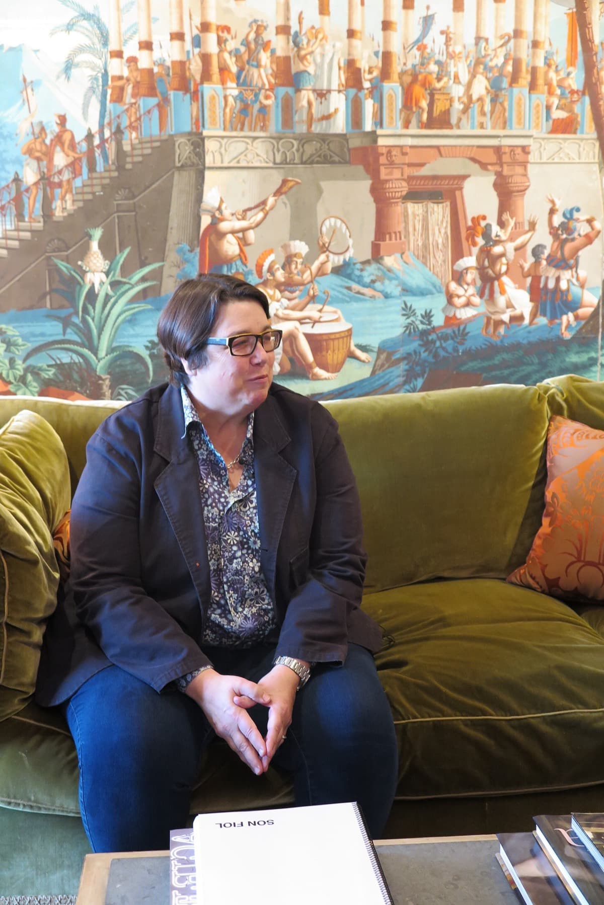Catherine Opie seated on a green sofa in front of a large painting