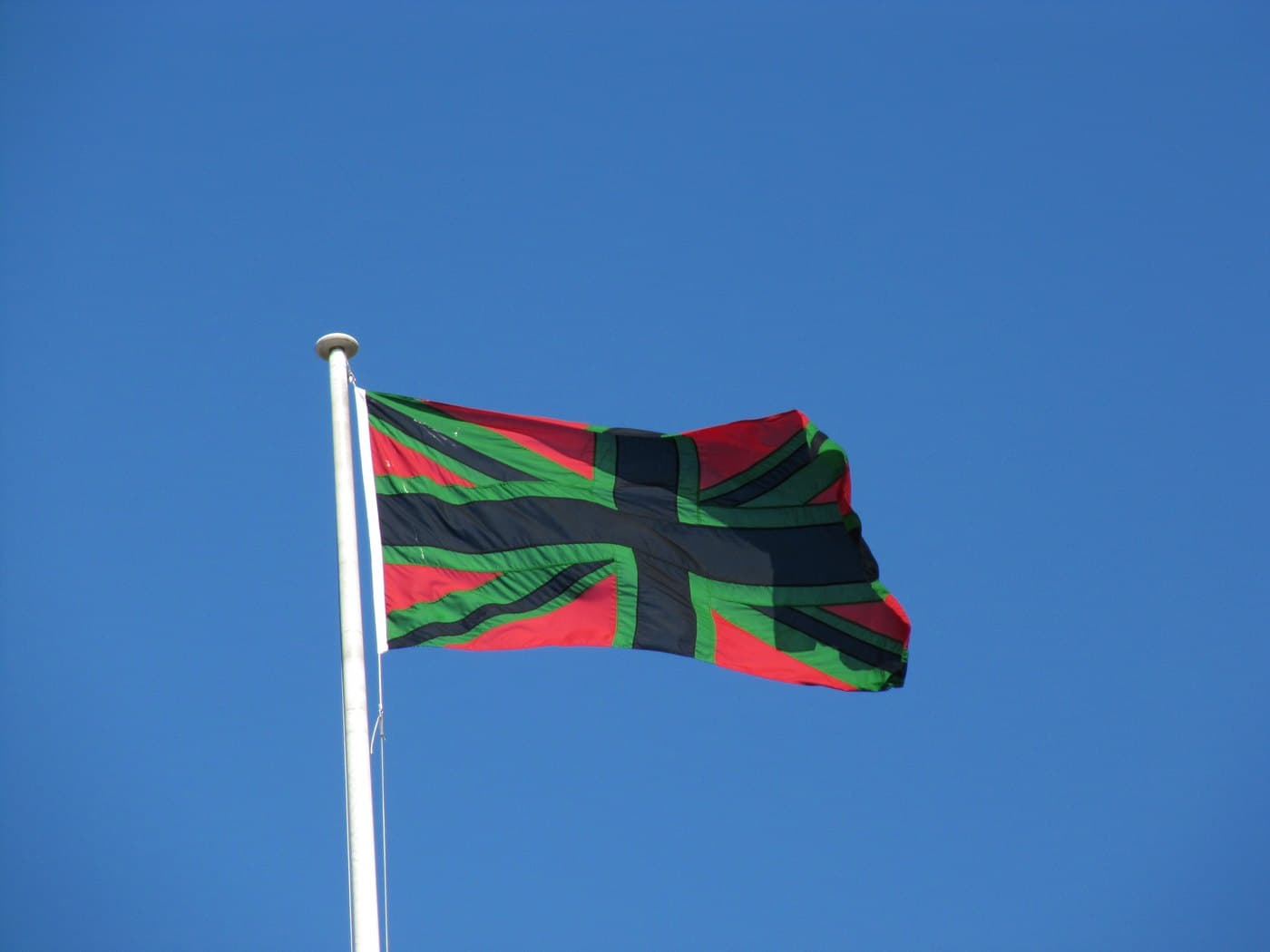Chris Ofili's Union Black, a Union flag in red, green and black, flying from a white flagpole against a clear blue sky at Tate Britain.