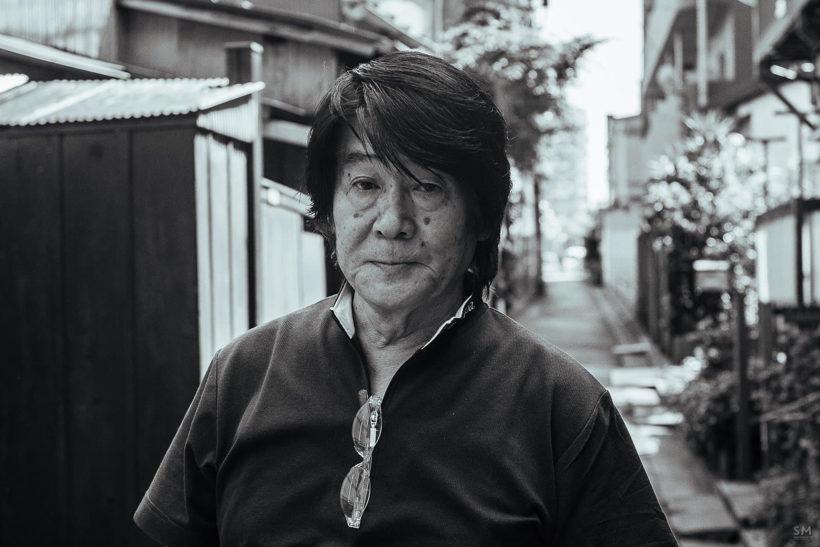 Daido Moriyama in a dark shirt on a narrow Tokyo street, in black and white