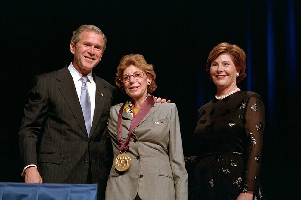 Helen Frankenthaler wearing a medal, standing between George W. Bush and Laura Bush on a stage.