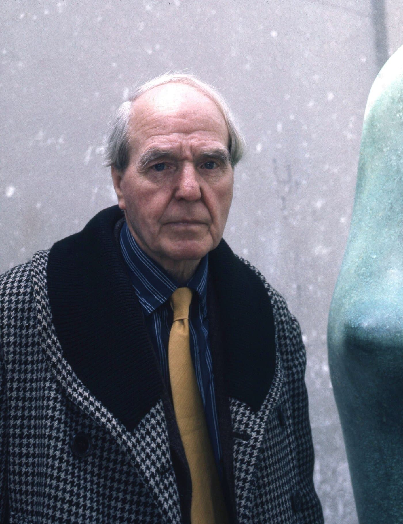 Henry Moore in a tweed jacket and tie, in his studio beside a sculpture.