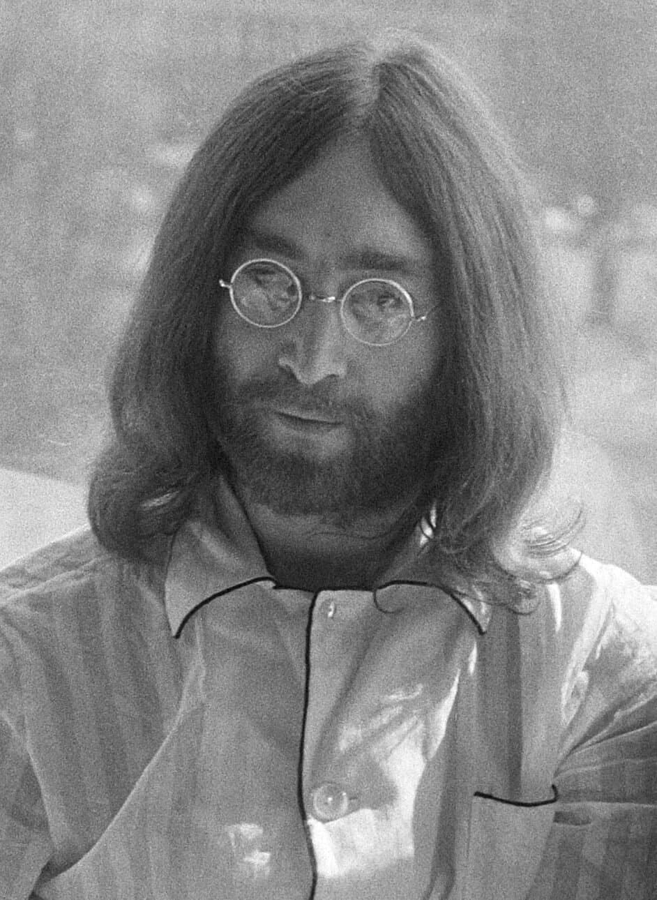 John Lennon with long hair, a beard and round wire glasses.