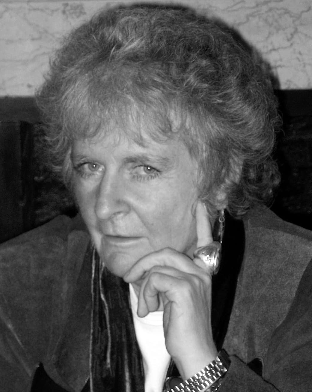 Maggi Hambling, chin on hand, with curly grey hair, in black and white.