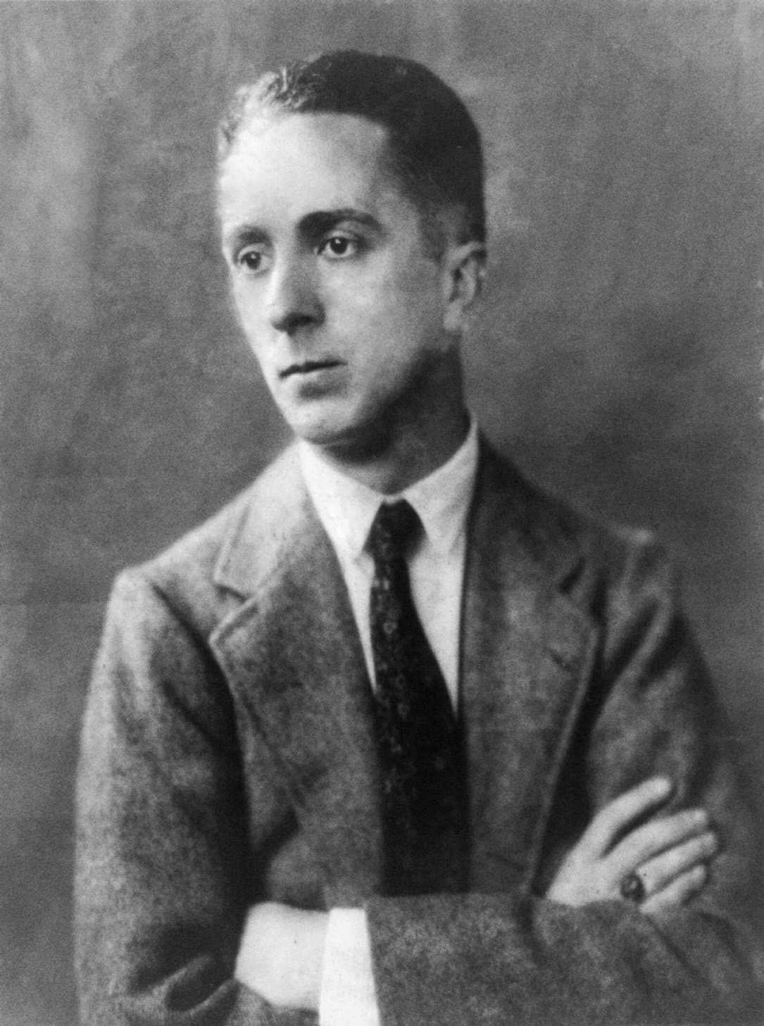 Norman Rockwell as a young man, in a jacket and tie, arms folded.