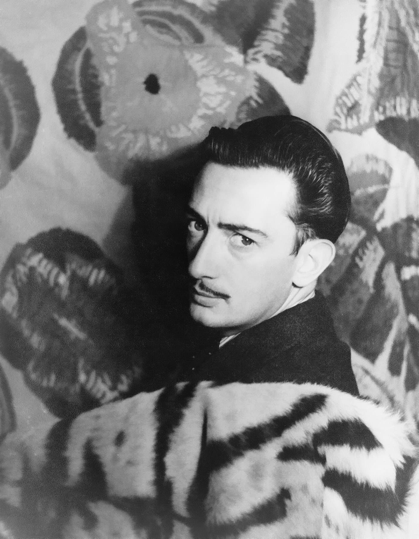 Salvador Dalí in profile, hair slicked back, against a patterned backdrop.