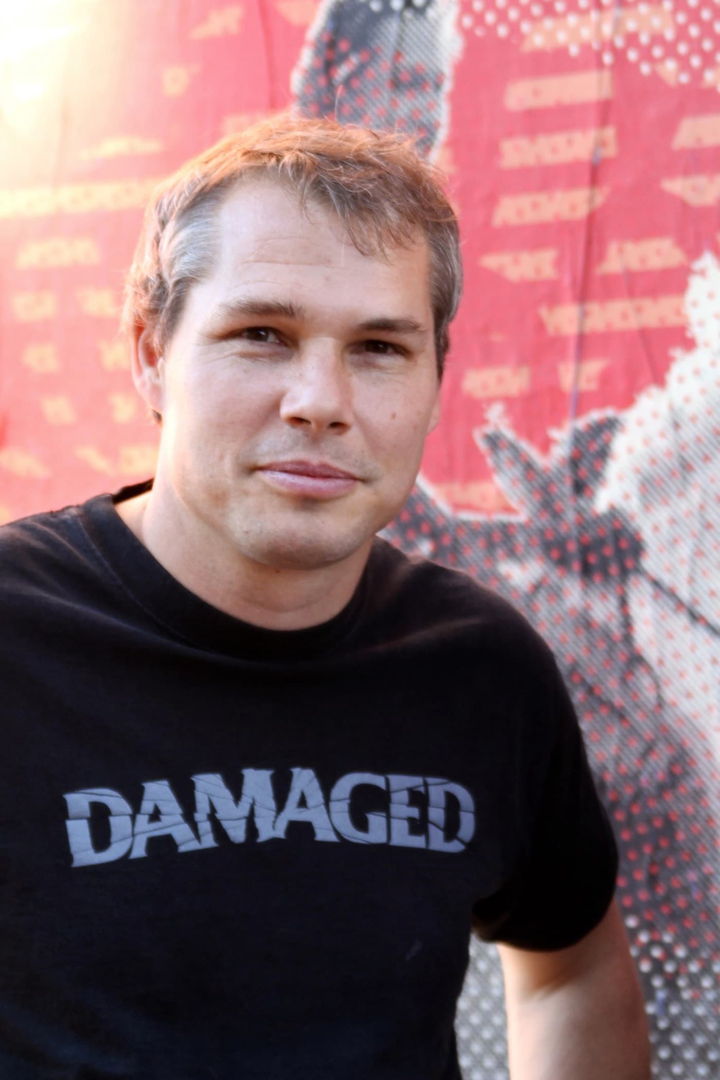 Shepard Fairey in a black T-shirt in front of a red and white mural.