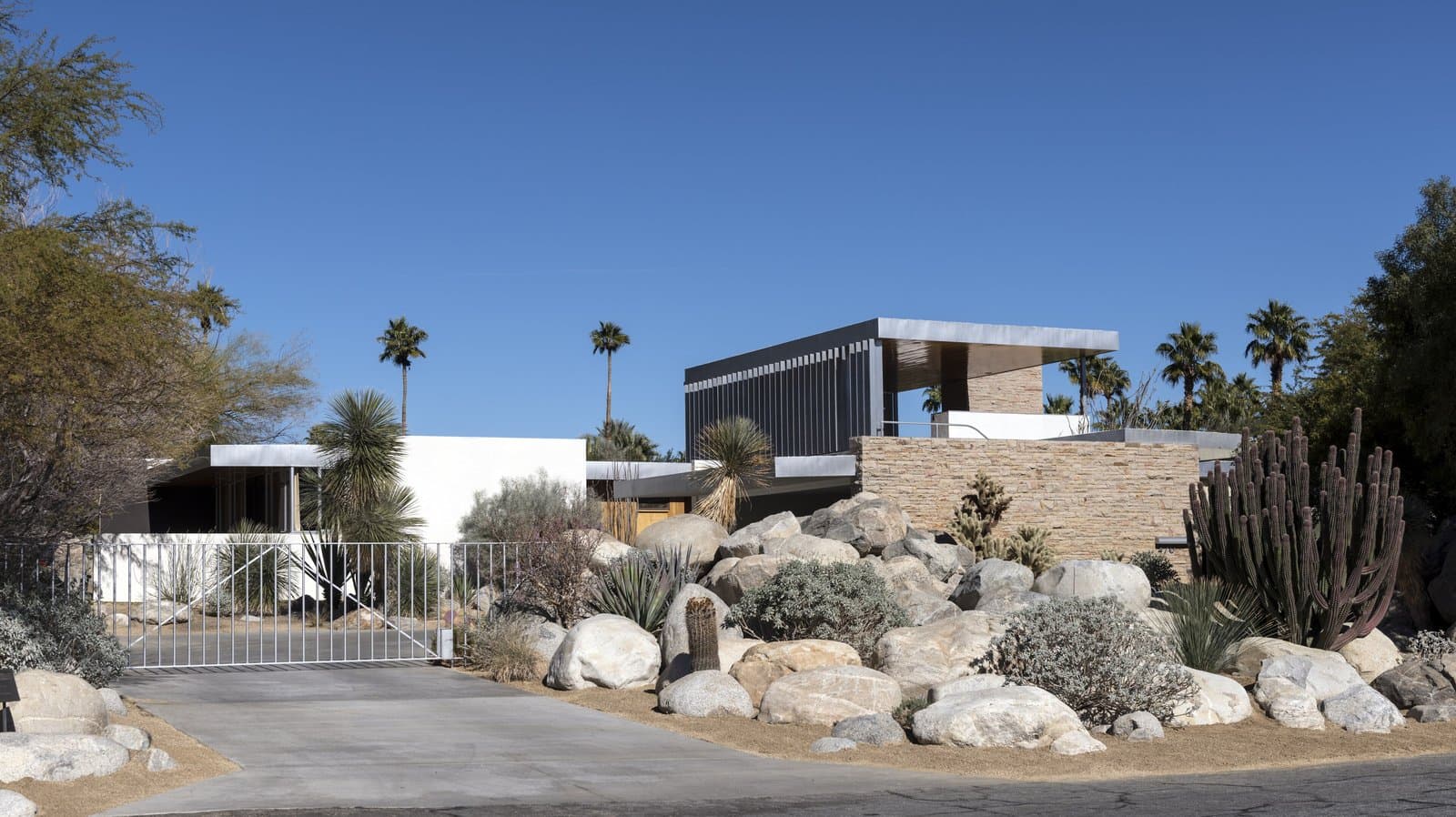 The low white Kaufmann house in Palm Springs behind a desert garden of rocks and cactus, under a blue sky