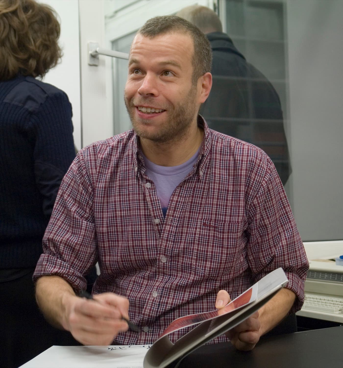 Wolfgang Tillmans in a checked shirt, smiling, in a gallery.