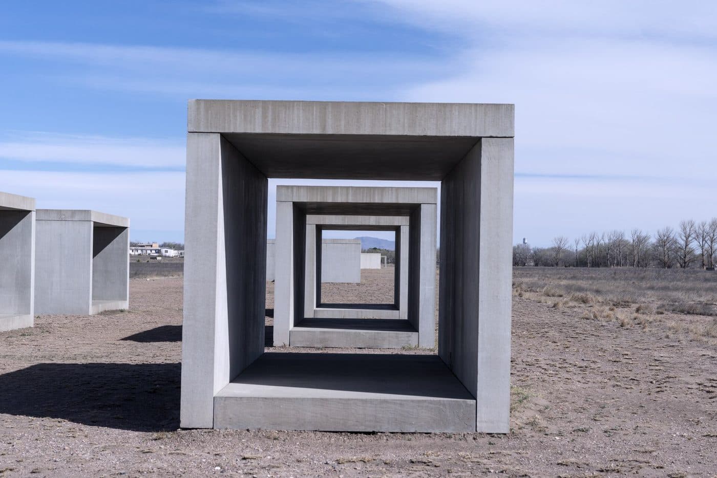 Open concrete boxes by Donald Judd standing in a line across dry grassland at the Chinati Foundation, Marfa, framing one another under a blue sky.