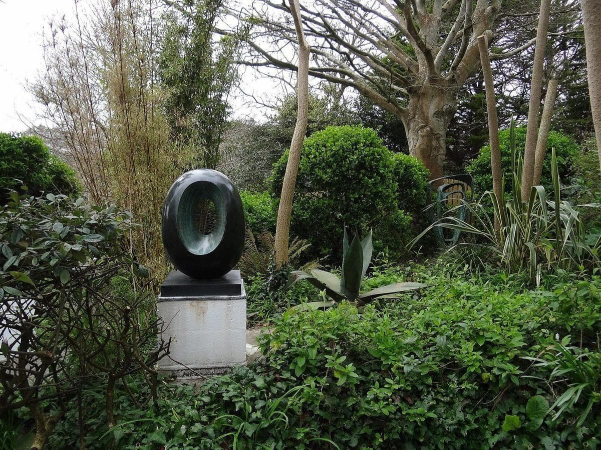 Barbara Hepworth's bronze Spring, an oval form pierced through the middle, on a plinth among the plants and trees of her garden in St Ives.