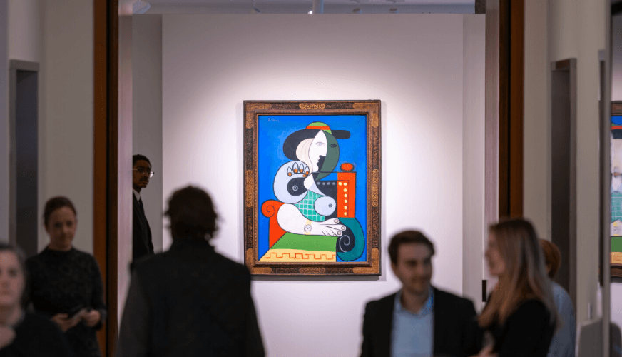 Visitors talking in front of a framed Picasso hung alone on a white gallery wall at a pre-sale view
