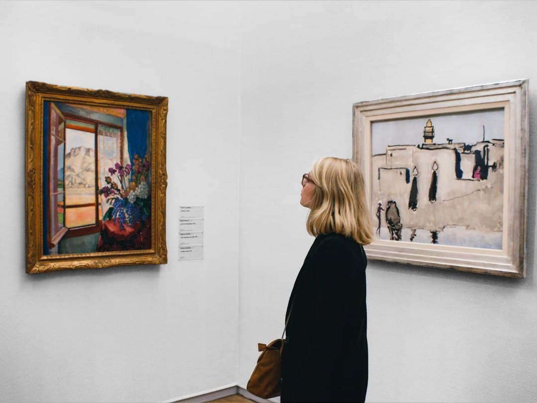 Visitor studying a framed painting beside its wall label in a gallery