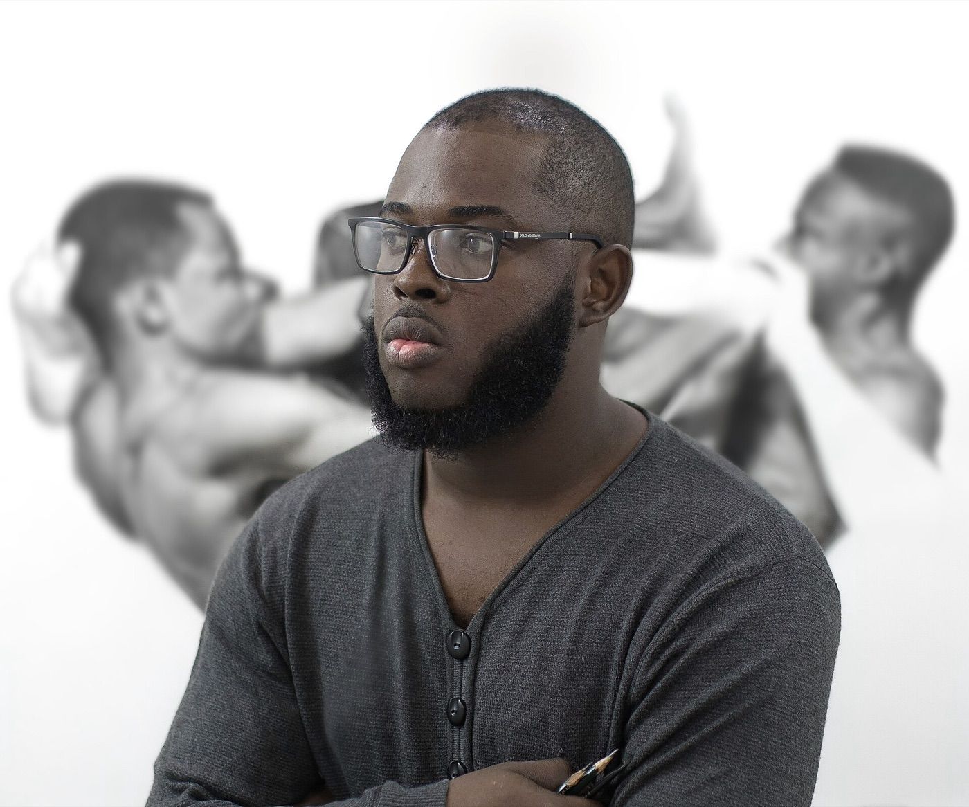 Arinze Stanley in glasses and a grey top, in front of his drawings of figures.