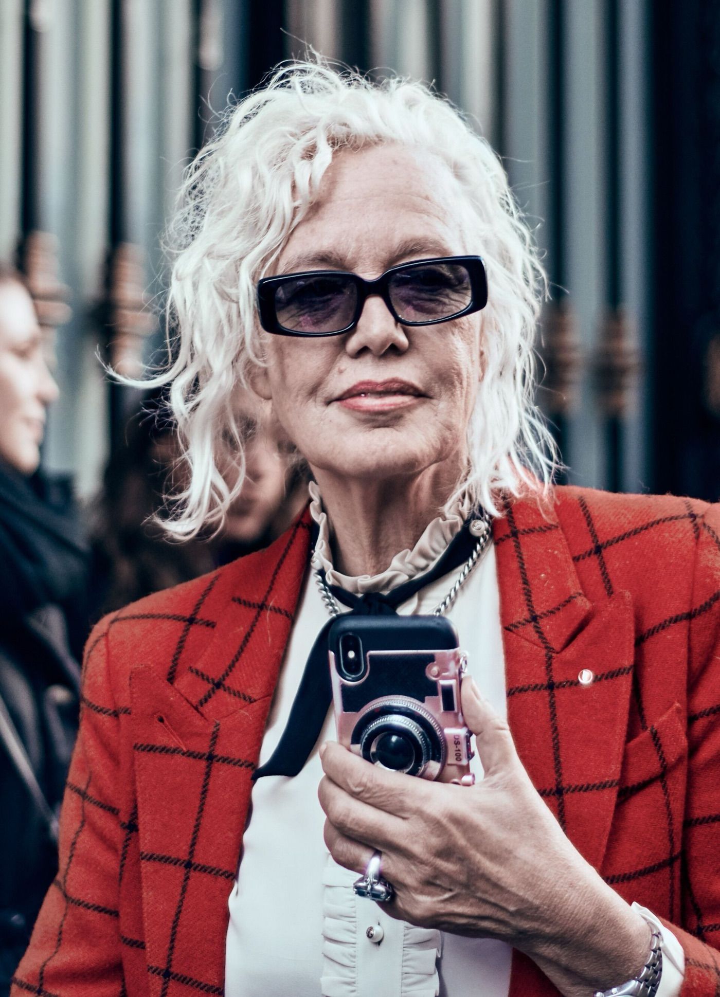 Ellen von Unwerth with white hair and dark glasses, in a red checked jacket.