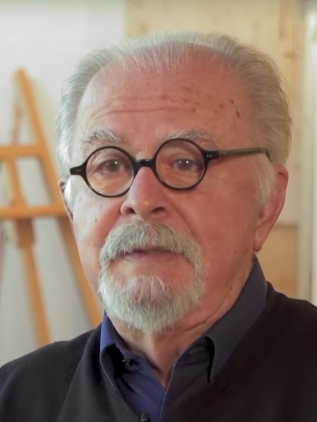 Fernando Botero with white hair, a moustache and round dark-rimmed glasses, in front of an easel.