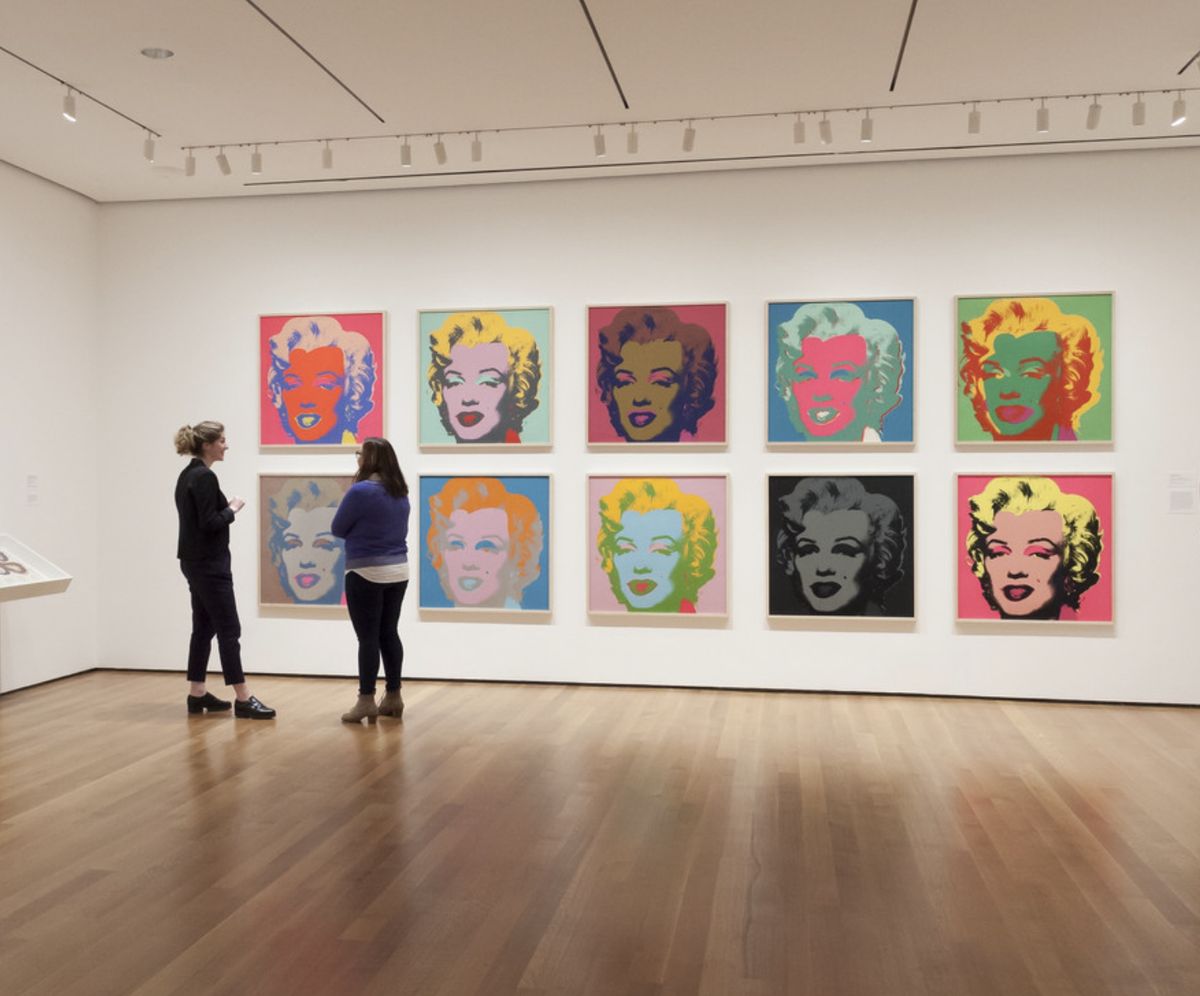 Ten Andy Warhol Marilyn Monroe screenprints in different colourways hung in two rows in a gallery, with two visitors talking in front of them